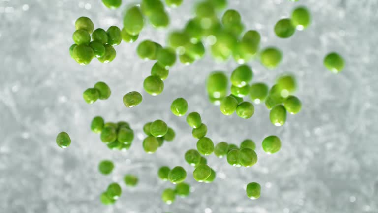 Green Peas Falling into Pot of Boiling Water Making a Splash in Slow Motion - Table Top View