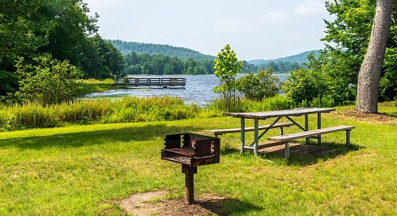 A metal barbeque grill and a picnic table at Chapman State Park in Clarendon, Pennsylvania, USA on a sunny summer day