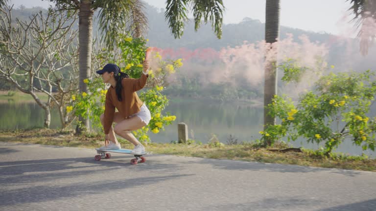 Asian women surf skate or skates board outdoors .