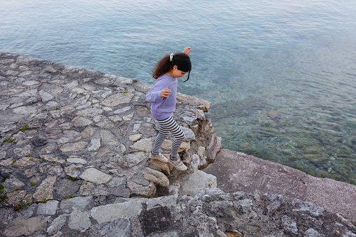 high angle view on girl in lilac top and striped pants jumping on the stairs next to the water of the lake