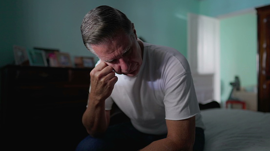 Stressed Middle-Aged Man Feeling Anxiety, Sitting by Bedside Depicting Mental Struggle and Preoccupation, suffering in quiet despair alone