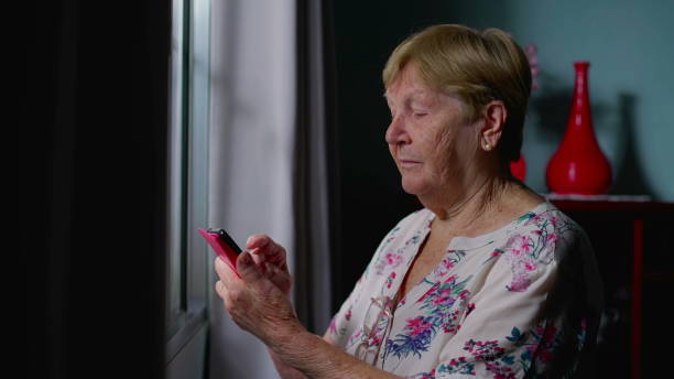 istock Senior Woman Using Smartphone by Window at Home, Elderly Person Typing Message, Intersection of Modern Technology and Old Age 1592416476