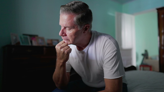 Stressed Middle-Aged Man Feeling Anxiety, Sitting by Bedside Depicting Mental Struggle and Preoccupation, suffering in quiet despair alone