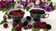 istock Raspberries and blackberries fall into cups with berries against the background of mallow flowers, slow motion 1592424309