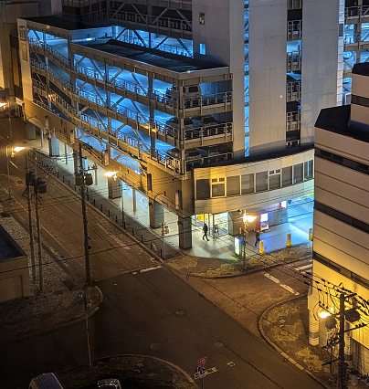 Kushiro City, Japan - June 5, 2023: Pedestrians walk past a downtown parkade lit up at night.