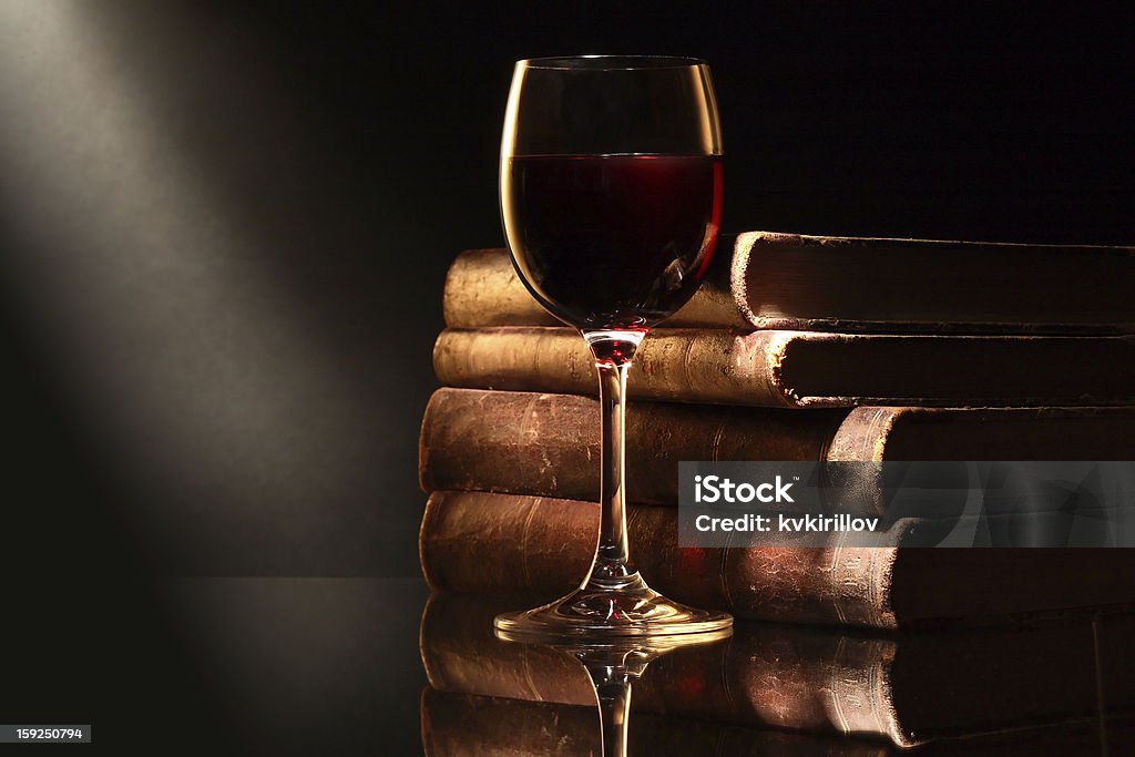 Wine And Books Elegant goblet of red dry wine near old books on dark background Book Stock Photo