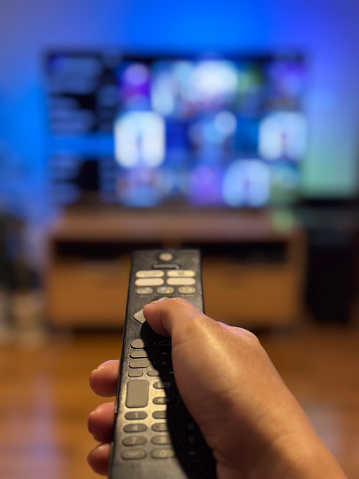 Person pointing a TV remote and pressing buttons in front of a TV with blank screen