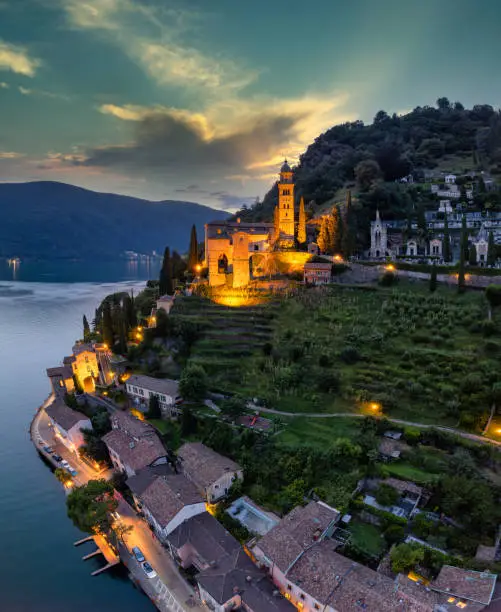 Aerial image of the parish church Madonna del Sasso stands on the high hill of Vico Morcote at sunset. Morcote at the Lake Lugano was once credited as one of the most beautiful Swiss villages.