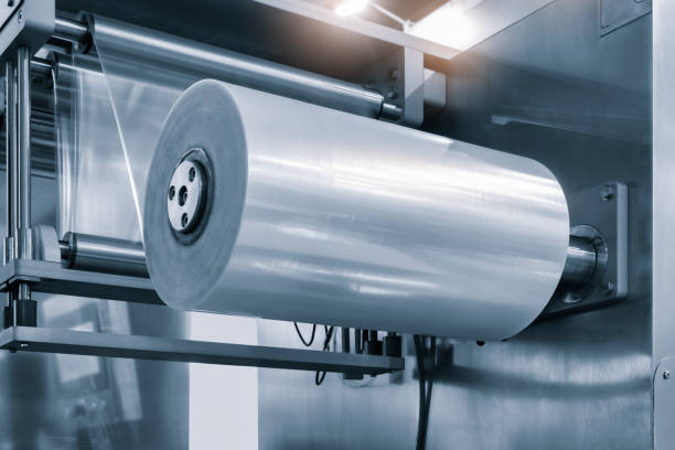 istock Automatic industrial machine for plastic packaging with light effect of products and food. shaft of an automated packaging line with plastic film in a light blue scene. product packaging concept 1592514339