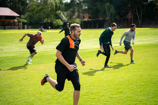 Group of people running on warm up exercise on sports field