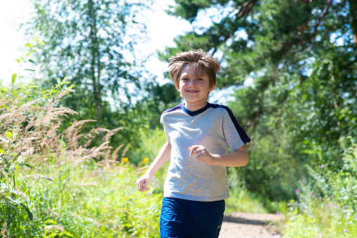 happy 10 year old boy runs along the forest road. joyful child runs on summer vacation in nature, in the park, on a sunny day.
