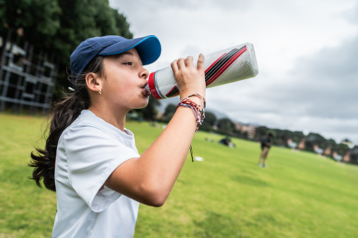 Child girl drinking water on the sports field