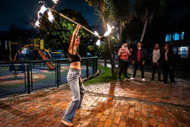 Photo of Mid adult fire juggler woman performing using flaming torch at night outdoors