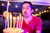 Mid adult man blowing out birthday candles on his anniversary at home