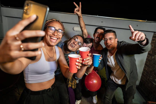 istock Young woman taking a selfie with her friends using a mobile phone on a party at rooftop 1592688607