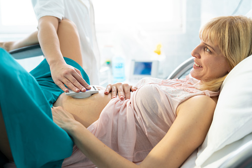 Smiling happy blonde woman doing ultrasound exam while waiting for the baby to be delivered. Joyful smiling pregnant woman having cardiotocograph in hospital.