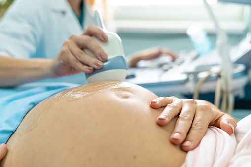 Woman at the doctor's office getting a checkup to ensure the health of her unborn child. Doctor is using a doppler device to ultrasound the woman's stomach to see the baby.