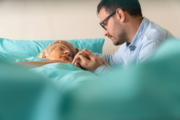Desperate young adult millennial man holding his mother's hand and head while she is sleeping in hospital bed Desperate young adult millennial man holding his mother's hand and head while she is sleeping in hospital bed. nervous holding hands stock pictures, royalty-free photos & images