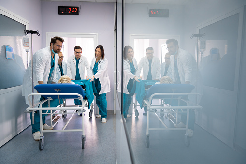 Group of male and female surgeons and doctors pushing unconscious patient on the bed into urgent surgery at hospital. Medical team in a hurry to save patients life.