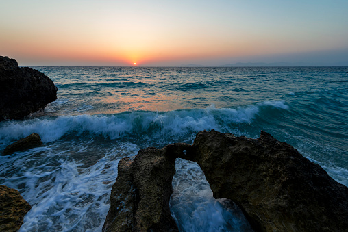 Waves crashing against rocks on coastline at sunset. Rhodes Island, Greece