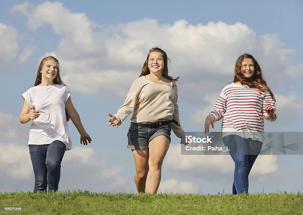 Tre sorridenti ragazze in esecuzione in verde erba - Foto stock royalty-free di Adolescente