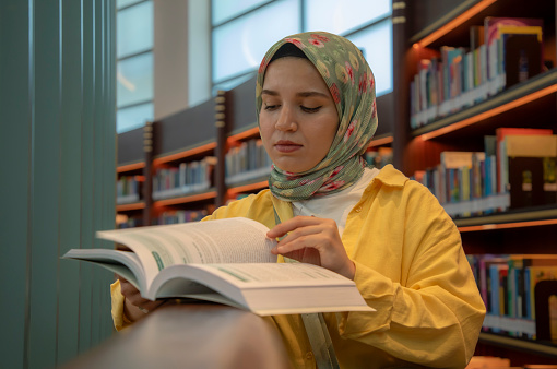 Young beautiful woman wearing a colorful headscarf examining a book in the library