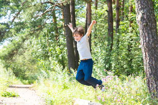 happy boy jumping over a log in the forest. 10 year old child jumps in the park in summer.