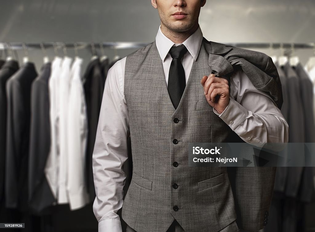 Uomo d'affari con un classico giubbotto contro la fila di abiti in negozio - Foto stock royalty-free di Uomini