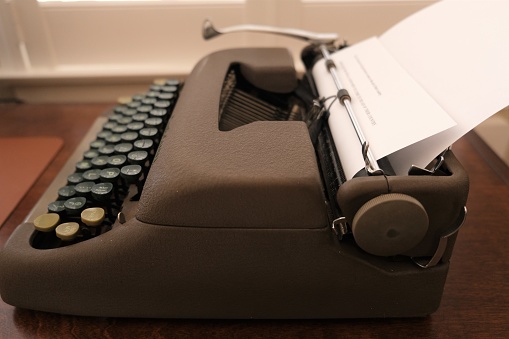Close up of 1940's manual typewriter from several different angles.  Typewriter sitting on a brown desk with light coming in through shutters.  Brown typewriter body with green keys.