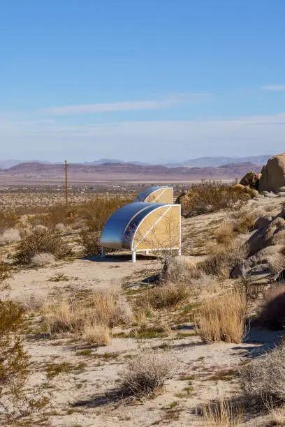 Two futuristic outdoor sleeping pods in the middle of the Mojave Desert of Joshua Tree, California. Mountains in the background. Vertical portrait shot.