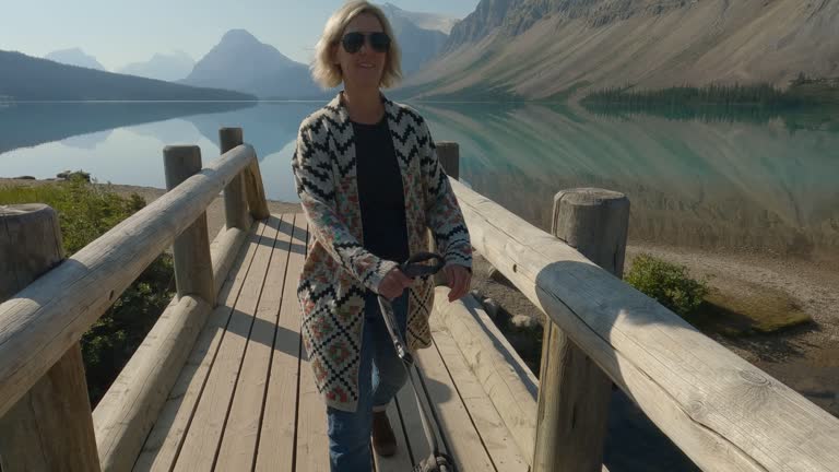 Woman walks dog on leash by mountain lakeshore, on bridge