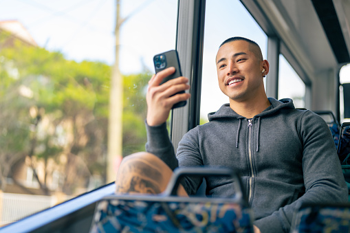 Asian man enjoy urban lifestyle using mobile phone and listening to the music on earphones during travel on bus in the city.