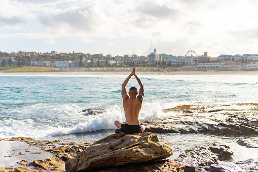 Asian man practicing meditation yoga exercise with ocean on coastline at summer sunset. Wellness health care, self motivation, outdoor lifestyle relaxing and nature therapy concept.