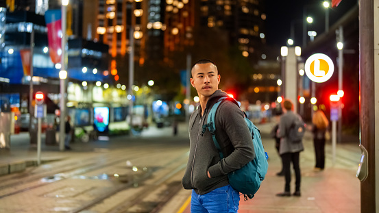 Confidence Asian man waiting for train at railway station in Sydney, Australia at night.
