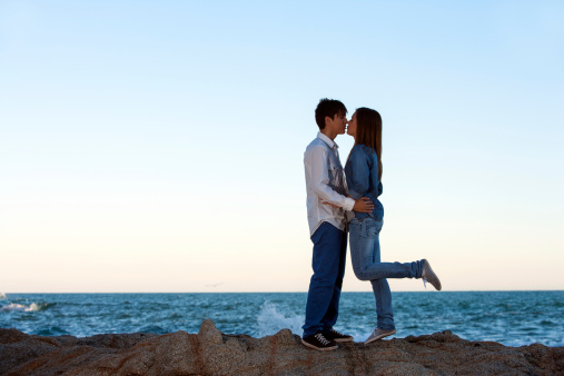 Romantic couple kissing on rocks at seaside.