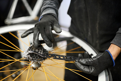 Maintenance of a bicycle: unknown man using protective gloves removing the cassette of a bike wheel at his repair shop. Concept: Small business owner at work.