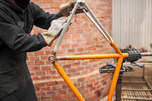 Unrecognizable worker using steel wool over a bicycle frame after passing a blowtorch over it to remove the paint, as part of his bike renovation work.