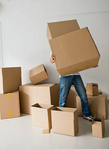 Man struggling to carry boxes while moving house.