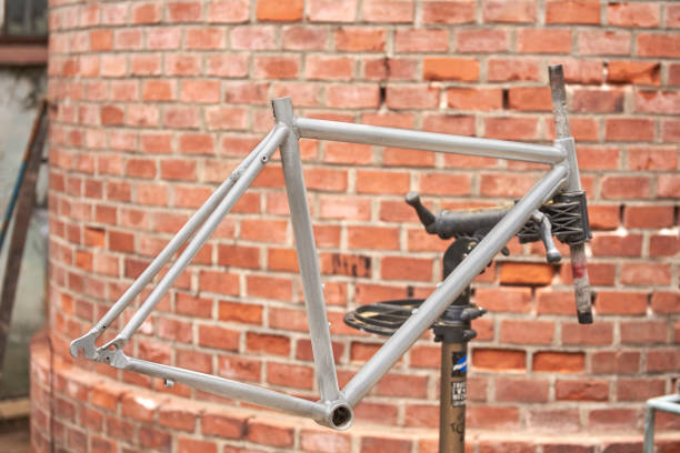 Unpainted silver bicycle frame held on a stand in a repair shop, in the process of renovation. Clean composition with copy space without people.