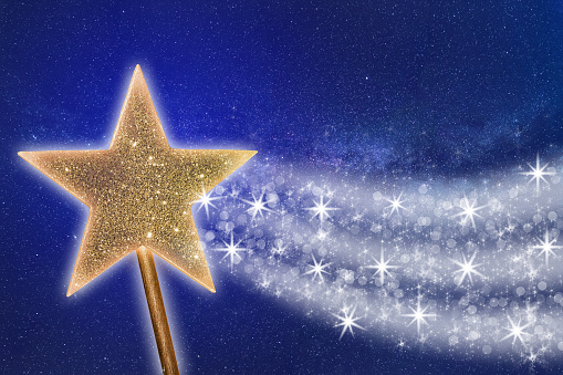 A golden magic wand leaves a sparkling trail of glowing white particles against a dark blue night sky.