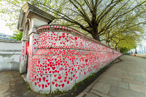 London, England, UK - May 8, 2023. The National Covid Memorial Wall in London visually represents, with hand painted red hearts, more than 220,000 UK victims of the Covid-19 pandemic. The Memorial Wall stretches for 500 meters alongside the River Thames, directly opposite the Houses of Parliament.