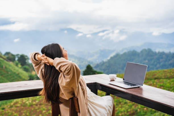 Young woman freelancer traveler working online using laptop and enjoying the beautiful nature landscape with mountain view stock photo