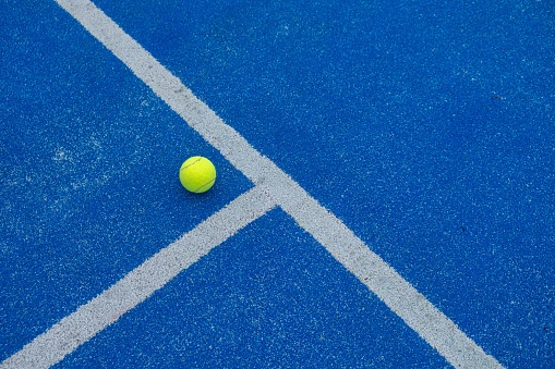 a ball on a blue paddle tennis court where the lines meet