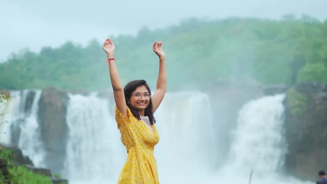 Portrait of teenager Indian girl raised her hands in front of flowing Gira waterfall at Saputara, Gujarat, India. Travel and holidays concept
