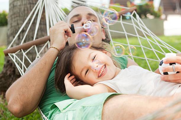 Father blowing bubbles and daughter smiling in a hammock  stock photo