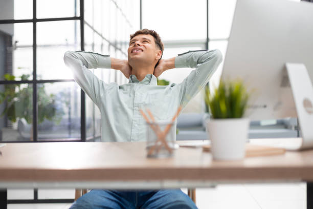istock Young modern businessman keeping hands behind head and smiling while sitting in the office. 1593486237