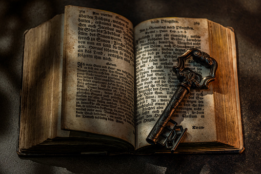 Ancient big key and opened book on dark background