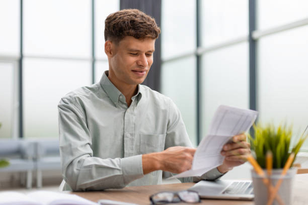 istock Young man is working with papers while sitting in the office. Successful entrepreneur is studying documents with attentive and concentrated look. 1593491395