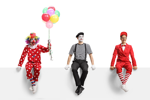 Male clown kissing female clown. Clowns with face painted wearing colorful costumes and wigs, white background.