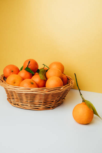 Orange mandarins clementine with green leaves in straw basket on a white-yellow background stock photo
